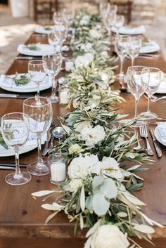 a long table with white flowers and greenery is set for an outdoor dinner party