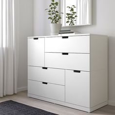 a white dresser with four drawers and a plant in the window sill next to it