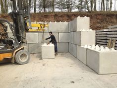 a man standing next to cement blocks in the middle of a construction area with a fork lift behind him