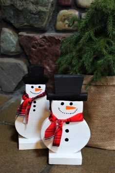 two snowmen are standing next to each other near a planter with a pine tree in the background