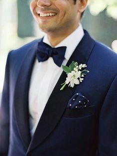 a man in a tuxedo smiles while wearing a flower boutonniere