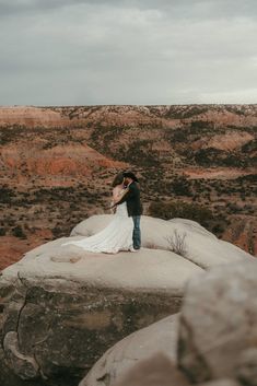 a man and woman standing on top of a large rock in the middle of nowhere