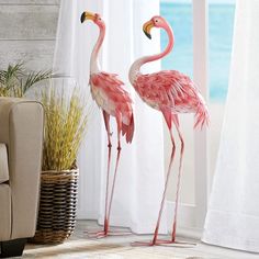 two pink flamingos are standing next to each other in front of a window with white curtains