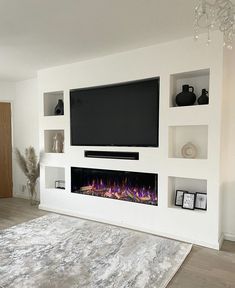 a living room with white walls and a fireplace in the center that has a large television mounted on it