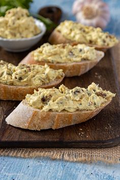 three pieces of bread on a cutting board with dip in the middle and vegetables behind them