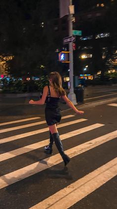 a woman in black dress and boots crossing the street with her legs spread out,