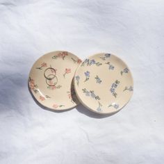 two plates with wedding rings on them sitting next to each other in front of a white background