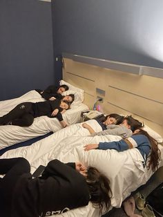 several people laying on top of beds in a room with blue walls and white sheets