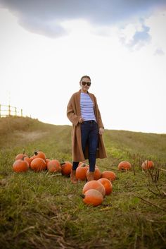 a woman standing in the middle of pumpkins on a field with her hands in her pockets