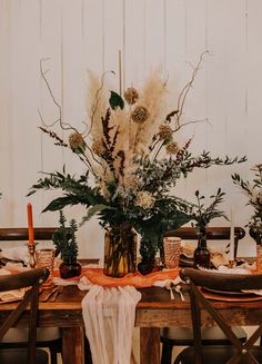 an arrangement of flowers and greenery on a table set for a dinner party with place settings