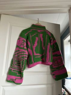 a green and pink sweater hanging on a door