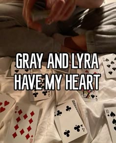 a person sitting on top of a bed with playing cards in front of him and the words gray and lyra have my heart