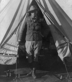 an old photo of a man standing in front of a teepee with the door open