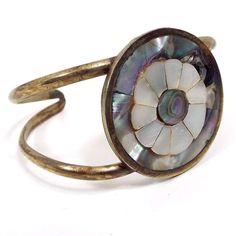 "Beautifully designed cuff bracelet with inlaid abalone and mother of pearl shell flower design.  Size:  1/4\" wide at it's widest point. Slightly adjustable with current opening of 2 1/8\". Type: Pre Owned Retro Vintage from the 1980's. Condition: Darkened patina on metal and some rub wear on the back where brass is showing through. All shell in good condition and no pieces missing. Not perfectly shaped, but you can gently reshape it to fit your wrist better. Materials: Silver tone alloy metal, mother of pearl shell, abalone shell. Markings: Marked Alpaca on the back." Adjustable Mother Of Pearl Bracelets As Gifts, Adjustable Mother Of Pearl Bracelet As Gift, Adjustable Mother Of Pearl Bracelets With Oyster Design, Adjustable Mother Of Pearl Bracelets For Gifts, Bohemian Adjustable Cuff Bracelet With Inlay, Mother Of Pearl Bangle Bracelets, Unique Adjustable Inlay Cuff Bracelet, Vintage Abalone Shell Jewelry For Gift, Vintage Silver Jewelry With Abalone Shell