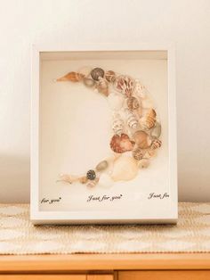 a white frame with seashells in it on top of a wooden table next to a wall