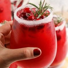 a hand holding a wine glass filled with red liquid and garnished with rosemary