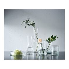 several vases with flowers and plants in them sitting on a glass table next to each other