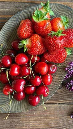 strawberries and cherries on a plate with lavenders next to them, sitting on a wooden table