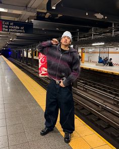 a man standing in front of a train at a subway station with his hand on his hip