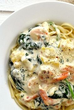 a white bowl filled with pasta covered in sauce and meat on top of spinach