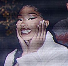 a woman smiling and holding her hands to her face while wearing a white shirt with an embellishment on it