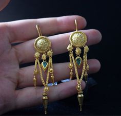 This 22 Karat Gold Emerald pair of earrings is inspired by ancient greek and Byzantine Jewelry. Handmade with love and craftsmanship, adorned with daisies, hand-wonen chain and 0.8 ct emeralds. Definitely a statement, this unique pair will steal the spotlight and everyones heart. In Ancient Greece, daisies were a symbol of purity, simplicity, and transformation. Daisies are composite flowers, meaning that they actually consist of two flowers combined into one. For that reason they symbolize true Historical Earrings, Greek Jewelry Goddesses, Ancient Greece Jewelry, Traditional Greek Jewellery, Greek Goddess Earrings, Greek Jewelry Ancient, Greek Earrings Ancient, Ancient Greek Jewelry Earrings, 22k Gold Earrings