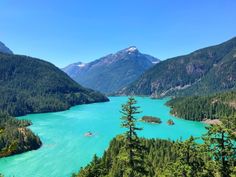 a lake surrounded by mountains and trees with blue water in the foreground on a sunny day