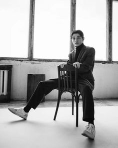 a young man sitting on top of a wooden chair in an empty room with large windows