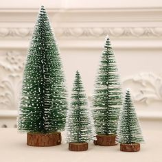 three small christmas trees in wooden stumps on a white table with ornate wallpaper