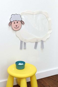 a sheep cut out on the wall next to a small yellow table with a cupcake