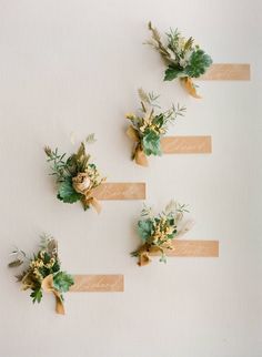 four boutonnieres with flowers and greenery are arranged on a white wall