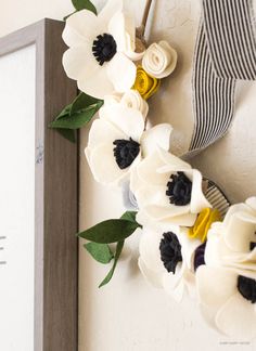 a white wreath with black and yellow flowers hanging on the wall next to a sign