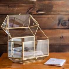 an open glass box sitting on top of a wooden table next to a notepad