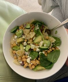 a white bowl filled with pasta, spinach and chickpeas on top of a green cloth