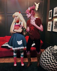 two women dressed in costumes standing next to each other near a red couch and chair