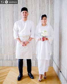 a man and woman standing next to each other in front of a wall with flowers