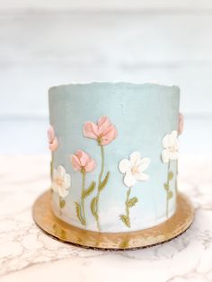 a blue cake with pink and white flowers on it sitting on a marble counter top