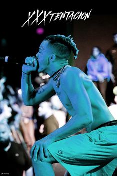 a young man with dreadlocks on his head is singing into a microphone in front of a crowd