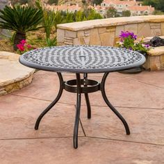 an outdoor table sitting on top of a patio next to a stone wall and flowers