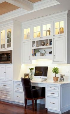 a kitchen with white cabinets and wood floors, along with a computer on the desk