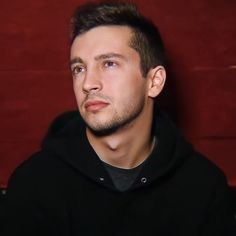 a man in a black hoodie looking at the camera with a serious look on his face