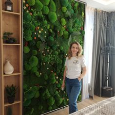 a woman standing in front of a living room wall with green plants on the walls