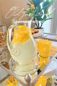 a glass pitcher filled with lemonade sitting on top of a table next to cookies