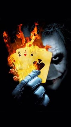 the joker holding two cards in his hand with fire coming out of it's face