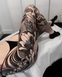 a woman laying on top of a bed with her legs crossed and flowers tattooed on her leg