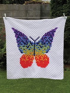 a butterfly quilt hanging on a clothes line in front of a brick wall and green grass