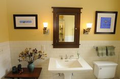 a white toilet sitting next to a bathroom sink under a wooden mirror mounted above it