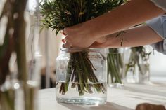 a person holding flowers in a jar on a table