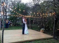 a bride and groom dance on a deck surrounded by string lights