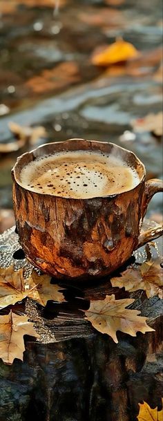 a cup of coffee sitting on top of a leaf covered table next to the water